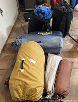 Overall lot of 6 camping items including sleeping bags and tents in storage bags on concrete floor.