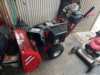 Overall view of red Troy-Bilt snowblower showing housing, controls and adjacent lawn mower.