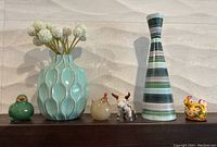 All items arranged on a shelf: two vases and four colorful animal figurines including a cow and roosters, one vase with a chip.