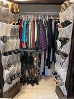 Closet view with hanging clothes on rack flanked by shoe organizers and shoes on floor