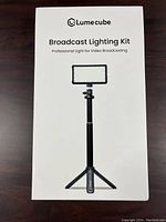 Front of white box showing Lume Cube Broadcast Lighting Kit with panel light on adjustable tripod stand.