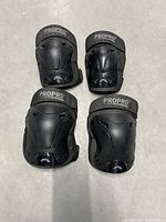 Set of 4 protective pads, two knee and two elbow pads with ProPro branding, showing front sides with hard plastic shells and Velcro straps.