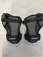 Front side view of two ProPro men's medium wrist protective pads in black and charcoal grey, showing mesh fabric and adjustable straps.