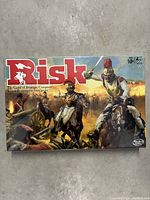 Front of unopened Risk board game box showing title and artwork of soldiers in battle on horseback.