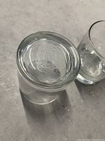 Bottom view of one clear thick bottom scotch glass showing subtle etched Celtic design on the base inside the glass.