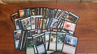 Photo of over 120 Magic The Gathering cards laid out on a wooden surface, showing a variety of cards from different sets and colors, all rare rarity.