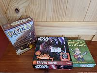 Photo showing all three board games: Giza The Great Pyramid sealed, Star Wars Trivia game, and Munchkin Cthulhu.
