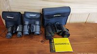 Three sets of binoculars displayed with their soft cases: two Tasco Mini Sport 4x30 and one Bushnell 8x30