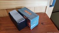 Boxed lot of 500+ Magic: The Gathering cards in a black plastic deck box with a 'Fate Reforged' themed cardboard sleeve next to it on a wood surface.