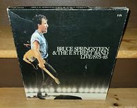 Front cover of the Bruce Springsteen & The E Street Band 5 LP box set showing Bruce with guitar on stage and stage lights below. Box shows minor wear and corner creasing.