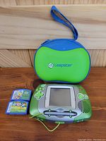 Photo showing green LeapFrog Leapster handheld system, two game cartridges, and blue-green carry case.