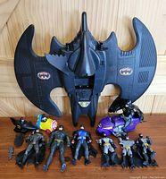 Top-down view of Batwing vehicle with Batman action figures laid out in front showing different figures and vehicle details.