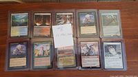 Top view showing all 10 Magic: The Gathering cards in plastic sleeves, laid out in two rows of five on a wooden surface.