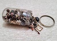Plastic container holding a variety of small broken jewelry, beads, chains, and pendants overflowing, shown next to a beaded bangle bracelet