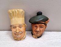 Image of both vintage chalkware wall heads together, displaying the Bossons chef on the left and Aquarian Art Scotsman on the right, showing paint wear and overall condition.