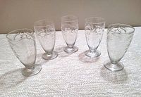 Five antique Glastonbury-Lotus crystal tumblers in a row on a light carpet, showing the etched leaf 'Majesty' pattern and footed bases.