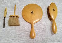 Five antique BIRKS vanity set items arranged in a row on fabric background including nail file, dust brush, handheld mirror, and hairbrush with French ivory handles.
