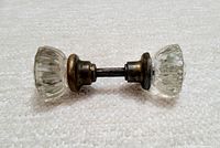 Full view of the antique crystal glass and brass door knob set laid horizontally showing both knobs, spindle, and brass fittings.