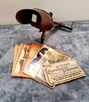 Photo of antique wooden stereoscopic viewer with several accompanying stereo view cards fanned out on a grey fabric surface.