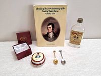 Photo showing full lot including commemorative book, empty whiskey bottle, two souvenir spoons, porcelain pin dish with lid and cushioned interior, and the original box for the dish.