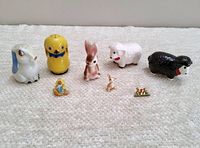 Vintage Easter-themed ceramic salt and pepper shakers and small collectible figurines and lapel pins displayed on fabric surface.