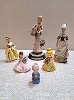 General front view of all six vintage Victorian women and girl figurines on white textured surface.
