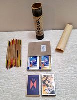 Photo of wooden pick up sticks, container, two decks of vintage playing cards in original packaging arranged flat with uncovered instruction sheet