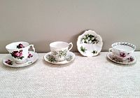 Four vintage Royal Albert teacup sets and one small dish displayed on a surface against a wall, showing floral patterns and gold trim.