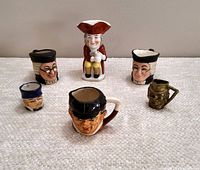 Group photo showing all six Toby jugs and mugs arranged in a semi-circle on a carpet.
