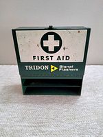 Front view of the metal first aid wall box with TRIDON branding and signal flashers text.