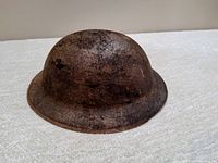 Side view of the rusted Brodie helmet showing wide brim and heavy surface corrosion.