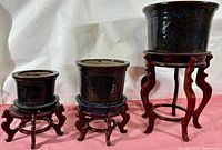 Front view of the three ceramic planters with underplates on wooden stands displaying their relative sizes and shapes.