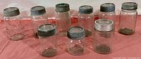 Wide view showing ten clear glass antique mason jars arranged in two rows, all with metal screw lids exhibiting age and patina. Jars vary in height approximately 5 to 7.5 inches.