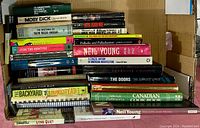 Photo of stacked books showing titles including Moby Dick, Ralph Waldo Emerson writings, Jimi Hendrix biography, and various cookbooks.