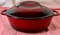 Front view of deep red enameled cast iron Dutch oven with lid closed, showing the overall shape and color.