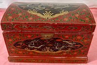 Front view of the red painted Chinese jewel casket showing dragon and floral decorations with metal clasp.