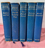 Five blue hardcover books with gold embossed spines showing titles and author Charles Dickens.