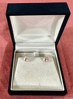 Pair of pearl stud earrings on sterling silver posts displayed inside an open black jewelry box with white fabric interior.
