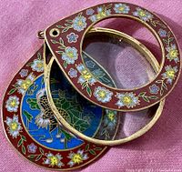 Close up of the loupe showing the cloisonne enamel floral pattern and the crane and lotus design on the inside panel, loupe open.