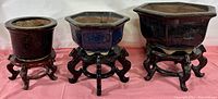 Photo showing the set of three pottery planter pots in varying sizes, each on a matching carved wood stand.