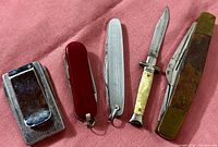 Five vintage pocket tools arranged on a red fabric background showing the variety of knives and tools included in the lot.