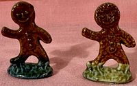 Front view of two gingerbread man figurines, one on dark green base, one on light green base, showing facial and button details.