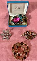 Four vintage rhinestone brooches arranged on a pink background, showing variety of designs and colors