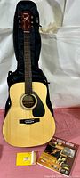 Full view of Yamaha acoustic folk guitar in soft black gig bag case with instruction book and yellow price tag
