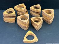 24 teak wood napkin ring holders stacked and grouped to show quantity and uniformity.