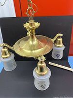 Chandelier side view showing brass arms and iridescent glass shades placed on a blue surface with orange background.