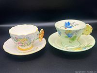 View of two teacup and saucer sets side by side showing butterfly handle cup and flower petal handle cup.