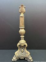 Front view of antique European bronze candlestick or lamp base showing fluted stem, ornate scroll base, and Catholic face motif.