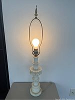 Full view of the antique white marble alabaster table lamp illuminated, showing overall shape and structure with harp and bulb.