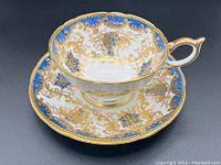 Close-up of Aynsley bone china cup and saucer set with gold gilt and blue grape pattern